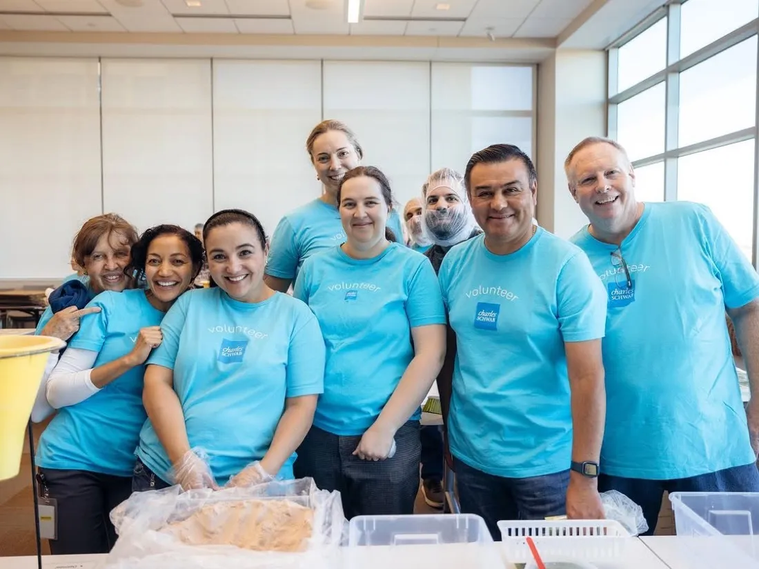 A team of smiling corporate volunteers in hairnets at a Harvest Pack packing table