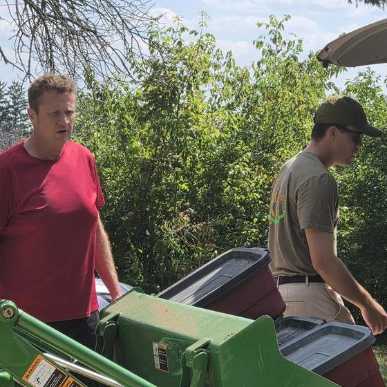 Helpers loading red bins of spilled ingredients onto the sanctuary tractor