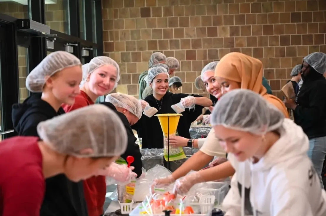 High school students smiling together while packing healthy meals at a Harvest Pack event